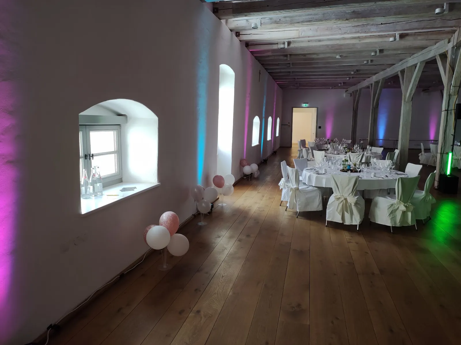 Saal im Wittelsbacher Schloss Friedberg mit Ambiente-Licht an den weißen Wänden und Tischen mit Hussen