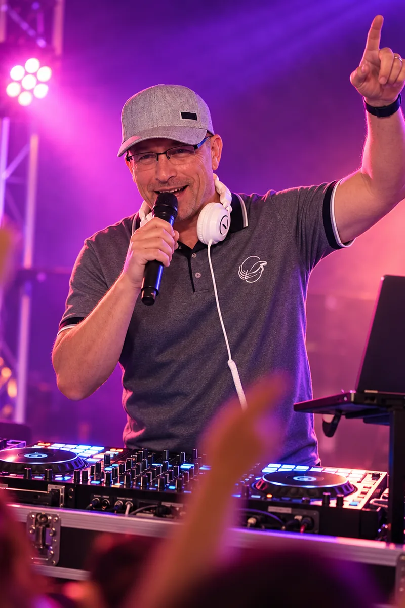 DJ Rico Cinsano mit Mikrofon am DJ-Pult bei einer Feier