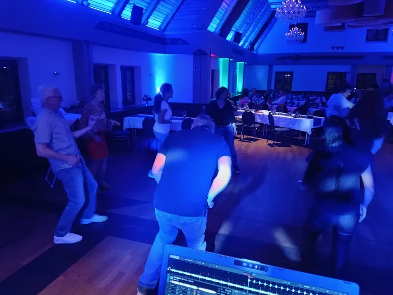 Tanzende Gäste im blau beleuchteten Saal des Strasser Gersthofen, im Vordergrund der Laptop am DJ-Pult