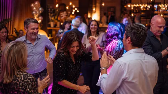 Lachende Gäste auf moderner Tanzfläche mit Sektgläsern, DJ für Geburtstag