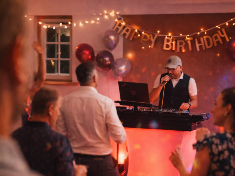 Geburtstags-DJ Rico Cinsano mit Mikrofon vor Happy-Birthday-Deko bei einer Geburtstagsparty