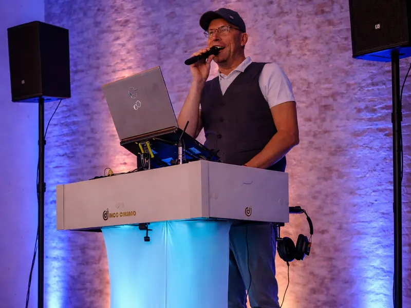 DJ Rico Cinsano mit Mikrofon am weißen DJ-Pult bei einer Firmenfeier