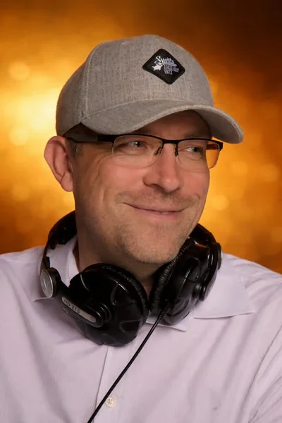 DJ Rico Cinsano mit Kopfhörern vor warm beleuchtetem Hintergrund