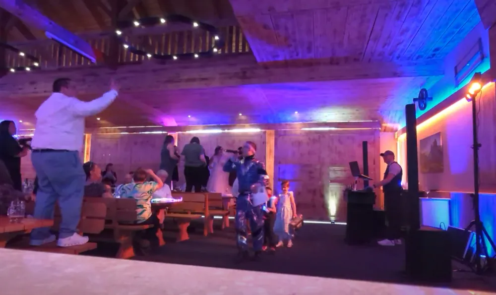 Stadel des Fischerwirt am Abend mit blauem und violettem Licht an den Holzwänden, Gäste und DJ-Pult