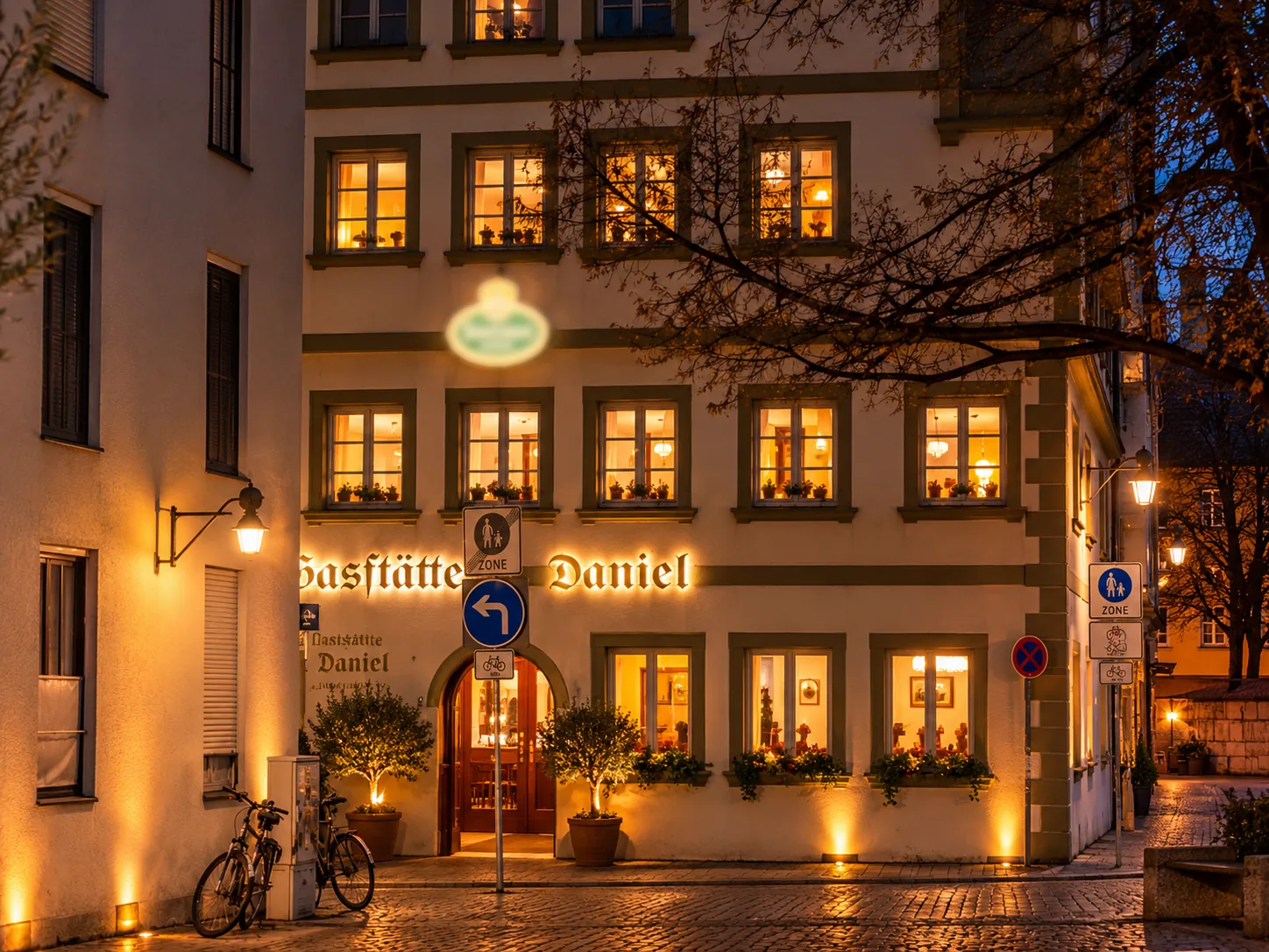 Gaststätte Daniel in Ingolstadt am Abend: beleuchtete Fassade mit Schriftzug, Rundbogentür und Fenstern mit Blumenkästen in der Altstadt