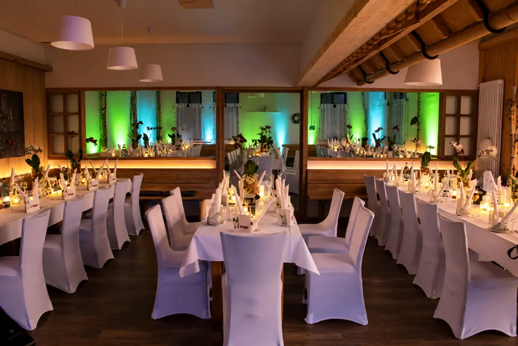 Saal der Schlemmerhütte mit Holzbalken, weißen Stuhlhussen und grün und blau beleuchteter Wand