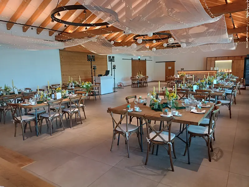 Grafenstadl Festsaal festlich gedeckt – runde Tische mit gelben Sommerblumen, DJ-Setup im Hintergrund und weißem Tülldach