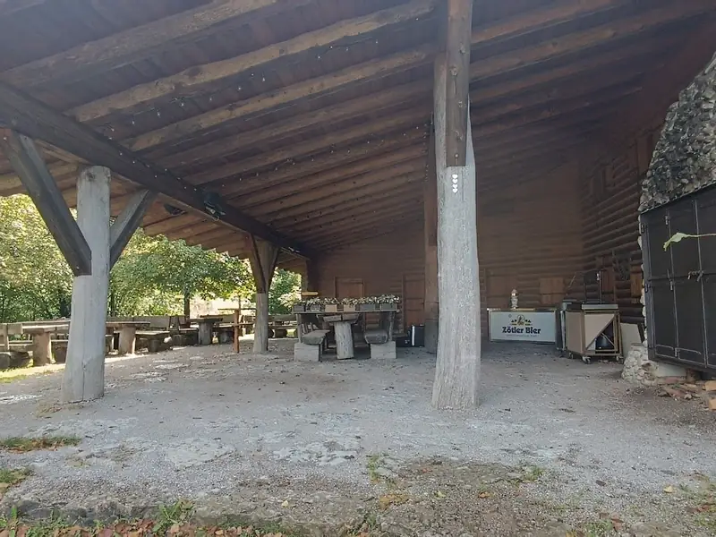 Überdachter Außenbereich der Sonnenkopfhütte mit Holzkonstruktion und Steinmauer